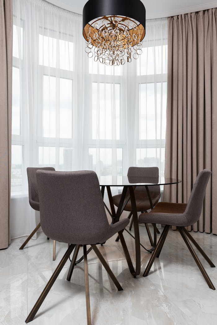 Home Chairs and table on floor under decorative chandelier against pleated curtains in contemporary house in daylight